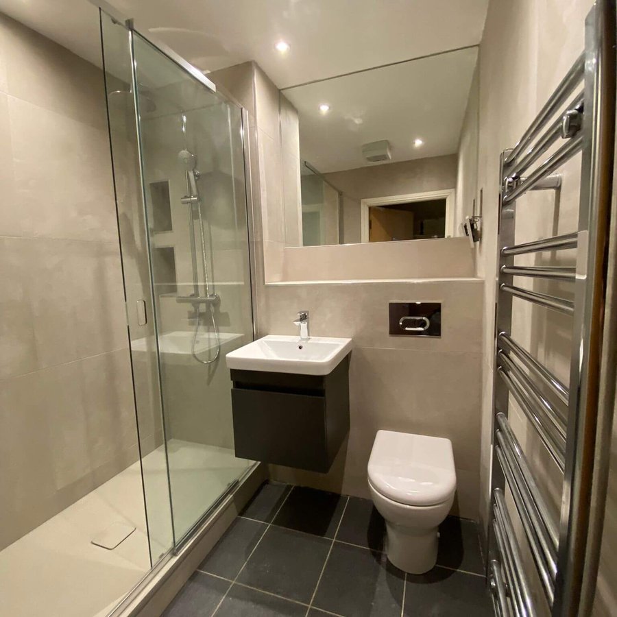 Modern shower room fitted by EcoGas with glass enclosure, wall-hung basin and chrome towel radiator